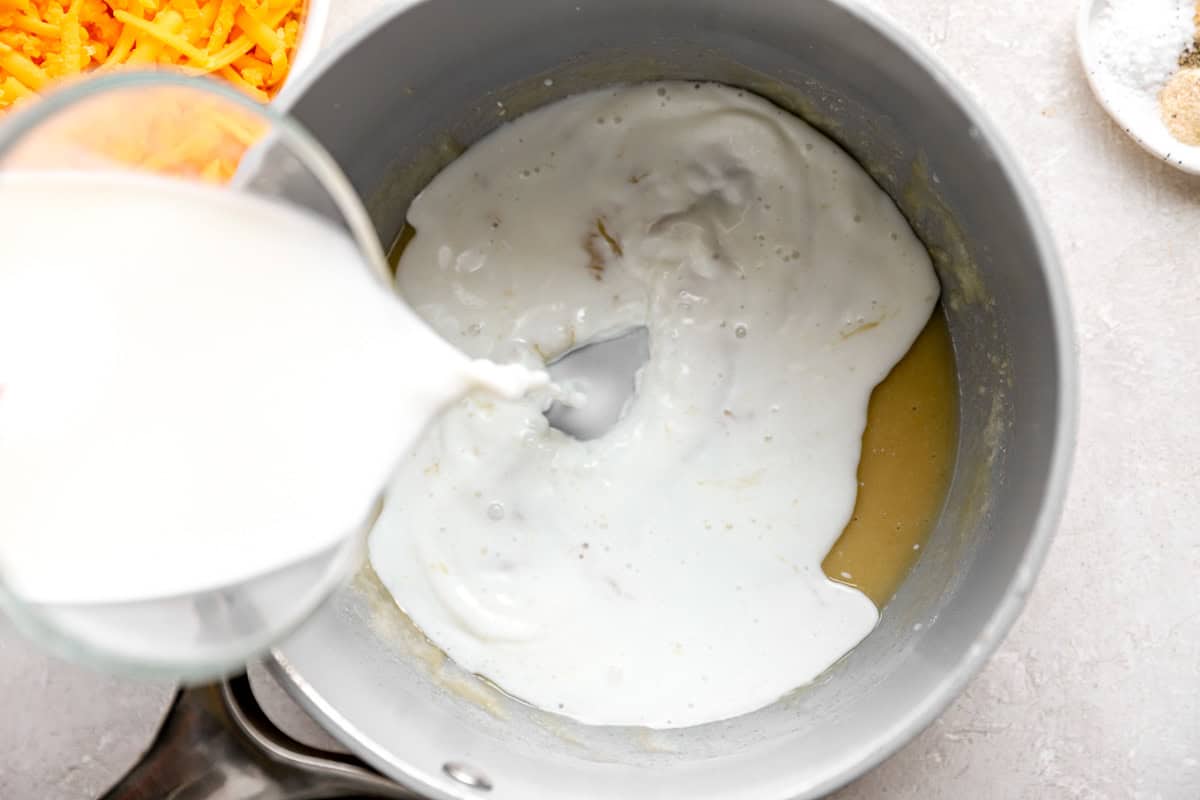 Milk being poured into a saucepan with the roux to start the cheese sauce base.