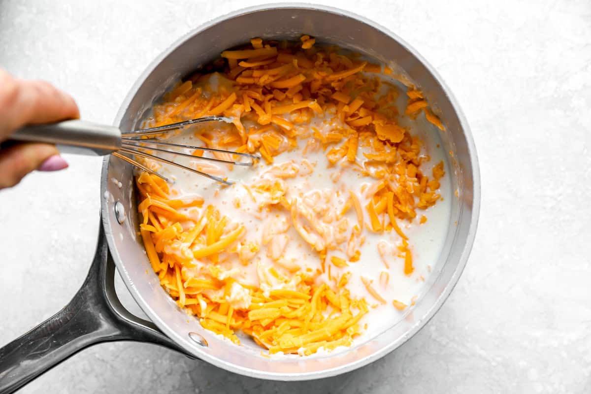 Shredded cheddar cheese added to the saucepan with the seasoned milk mixture.