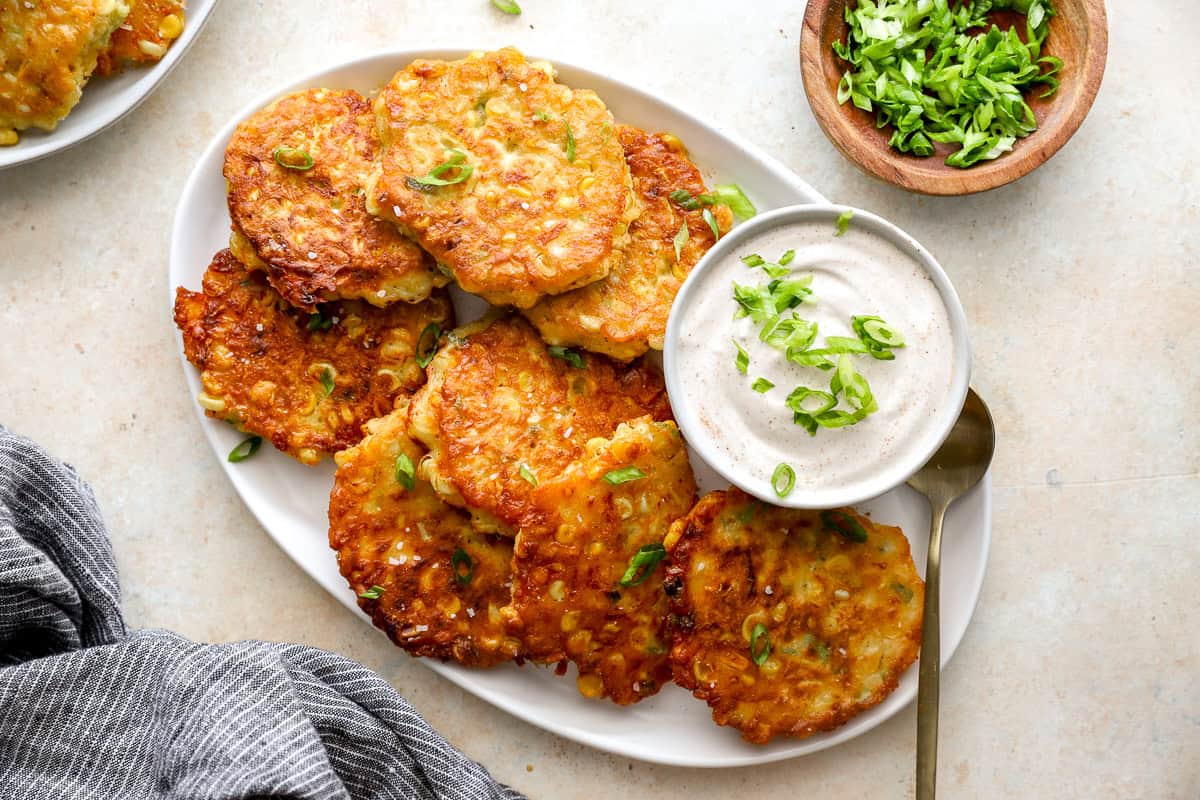 Crispy corn fritters on a platter with sour cream dip, garnished with fresh green onions.