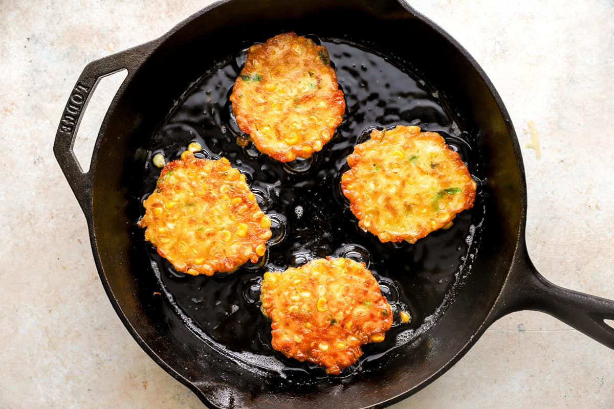 Golden corn fritters sizzling in hot oil in a cast iron skillet.