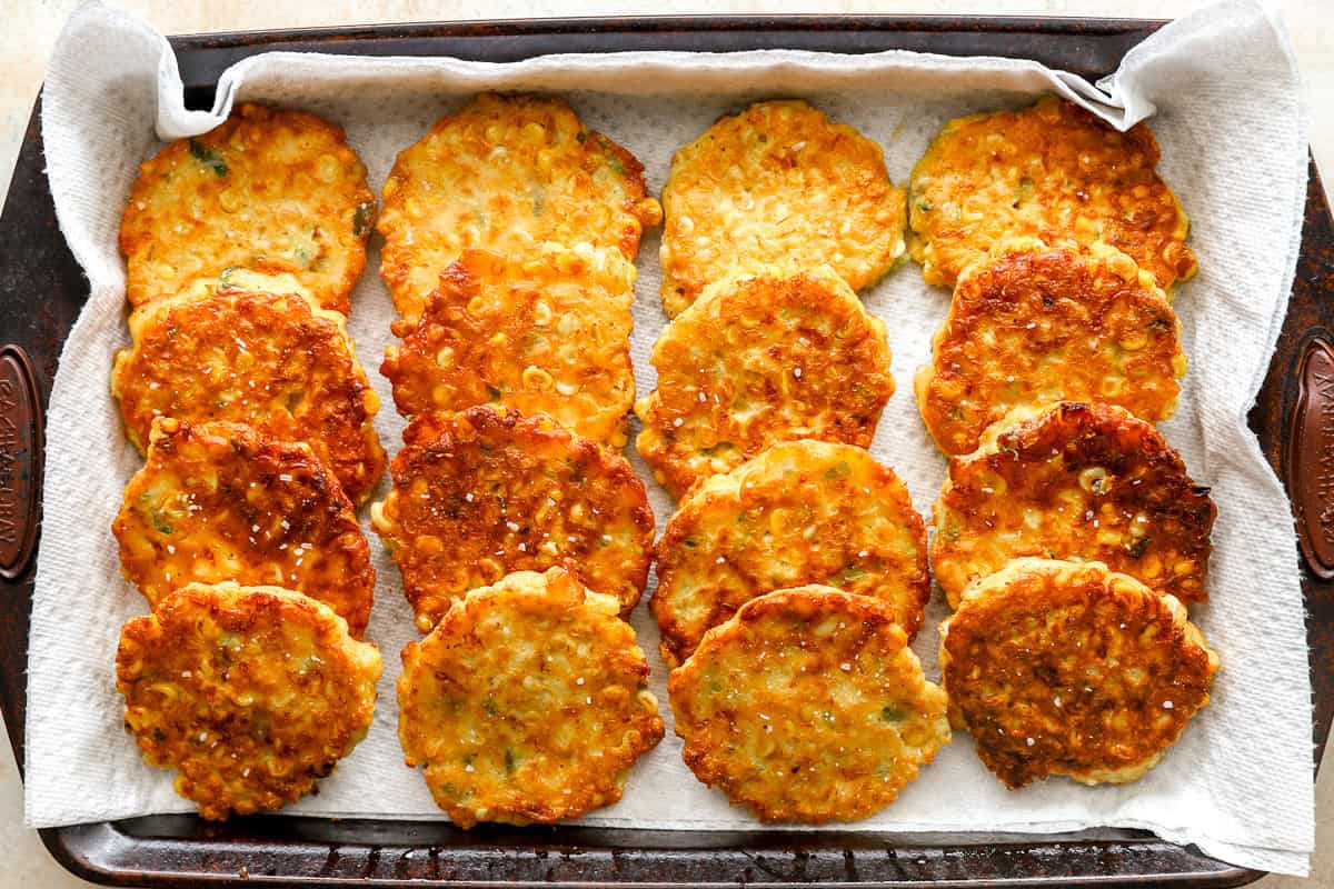 Freshly fried corn fritters draining on paper towels in a baking pan.