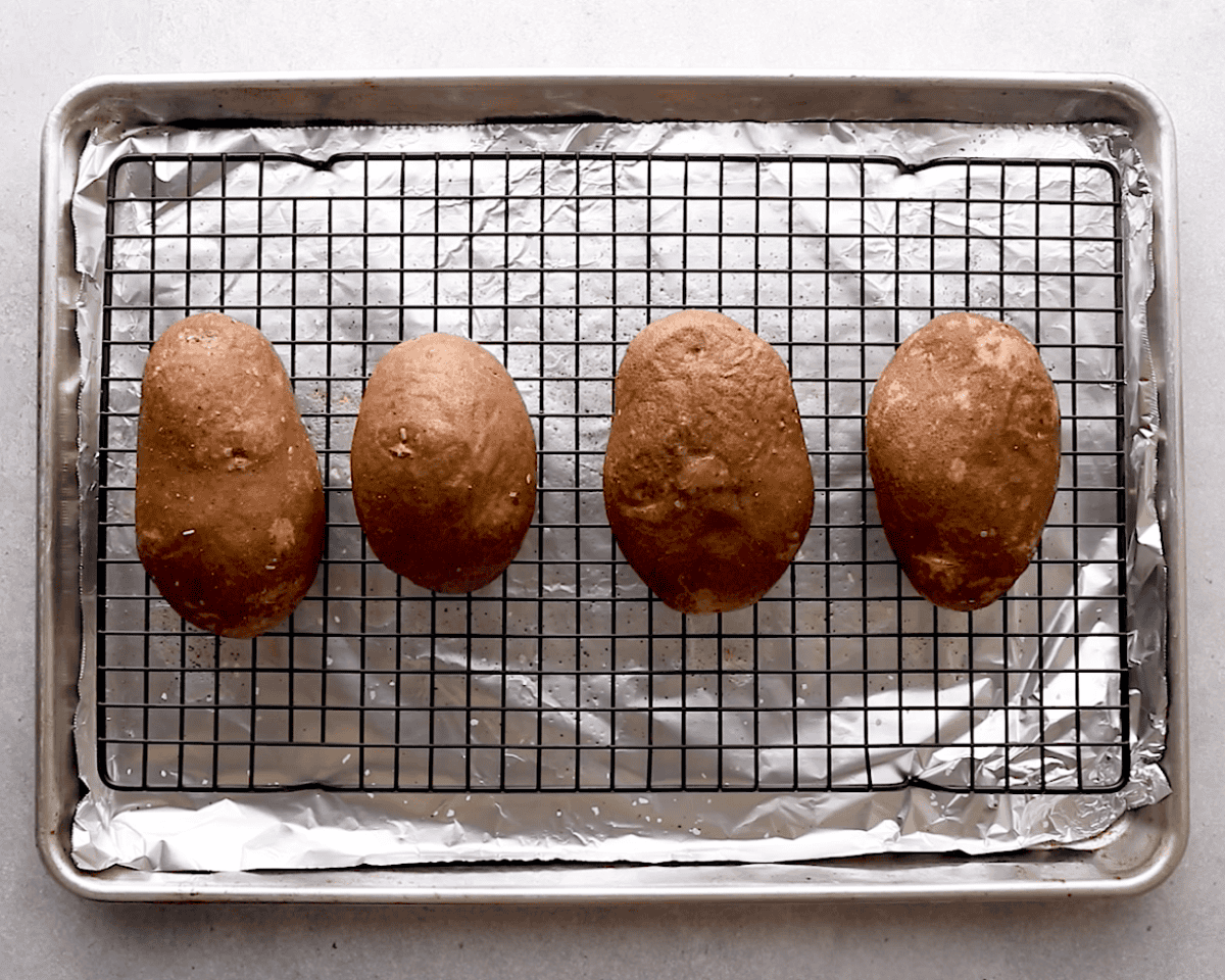 Baked Russet potatoes on a wire rack over a foil-lined sheet pan after the first bake.