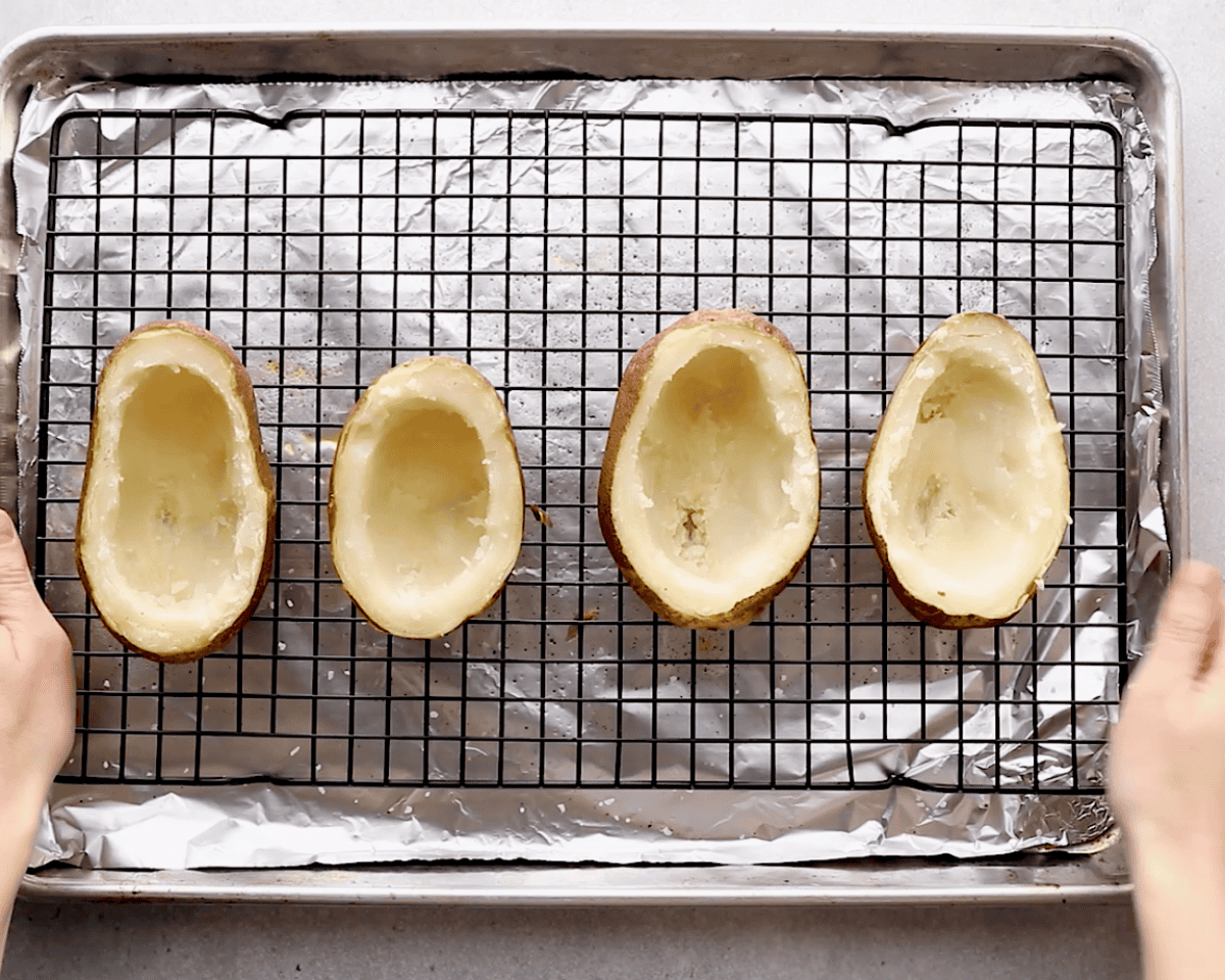 Four potato shells arranged on a wire rack over a baking sheet, ready for the second bake to crisp the skins.