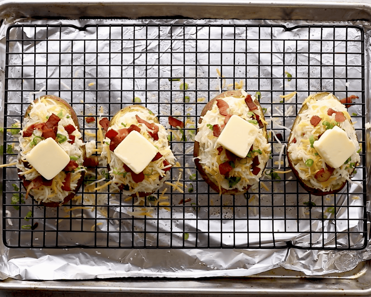 Potato shells filled with mashed potato mixture, topped with shredded cheese, bacon, scallions, and a pat of butter on each.
