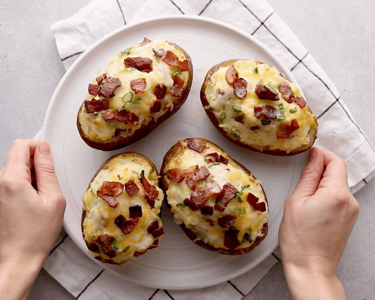 Finished twice baked potatoes on a white plate, topped with melted cheese, crispy bacon, and scallions.