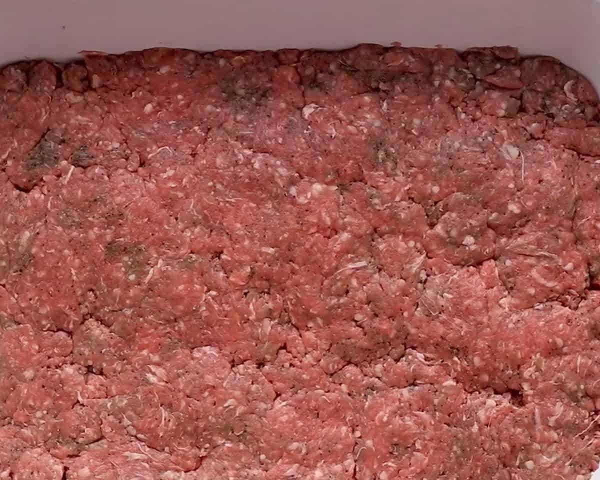 Ground beef patted down into a baking pan.