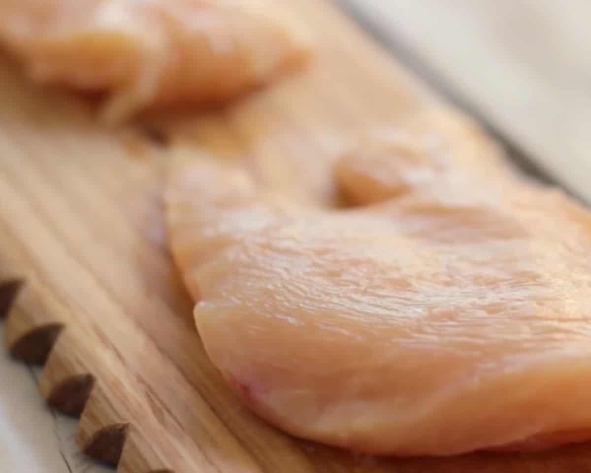 Raw boneless skinless chicken breasts on a wooden cutting board, trimmed and sliced in half - 6