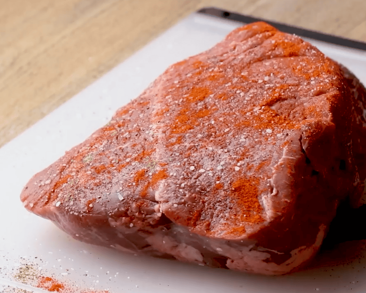 Raw chuck roast on a cutting board coated with salt, pepper, and paprika, ready to be seared.