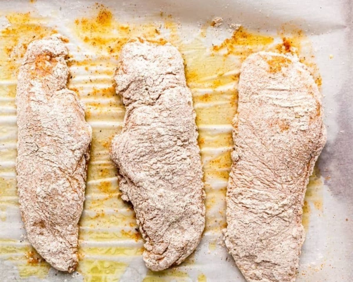Chicken breasts coated in seasoned flour mixture arranged on a buttered baking sheet - 10