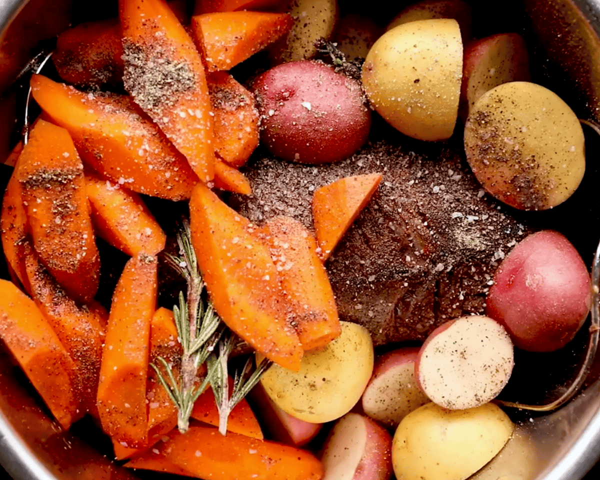 Pot roast with carrots and baby potatoes seasoned with salt and pepper before final cooking.