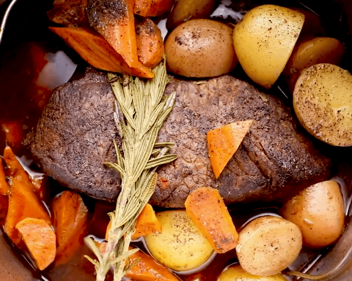 Cooked Instant Pot pot roast with carrots, potatoes, and rosemary in the pot after pressure cooking.