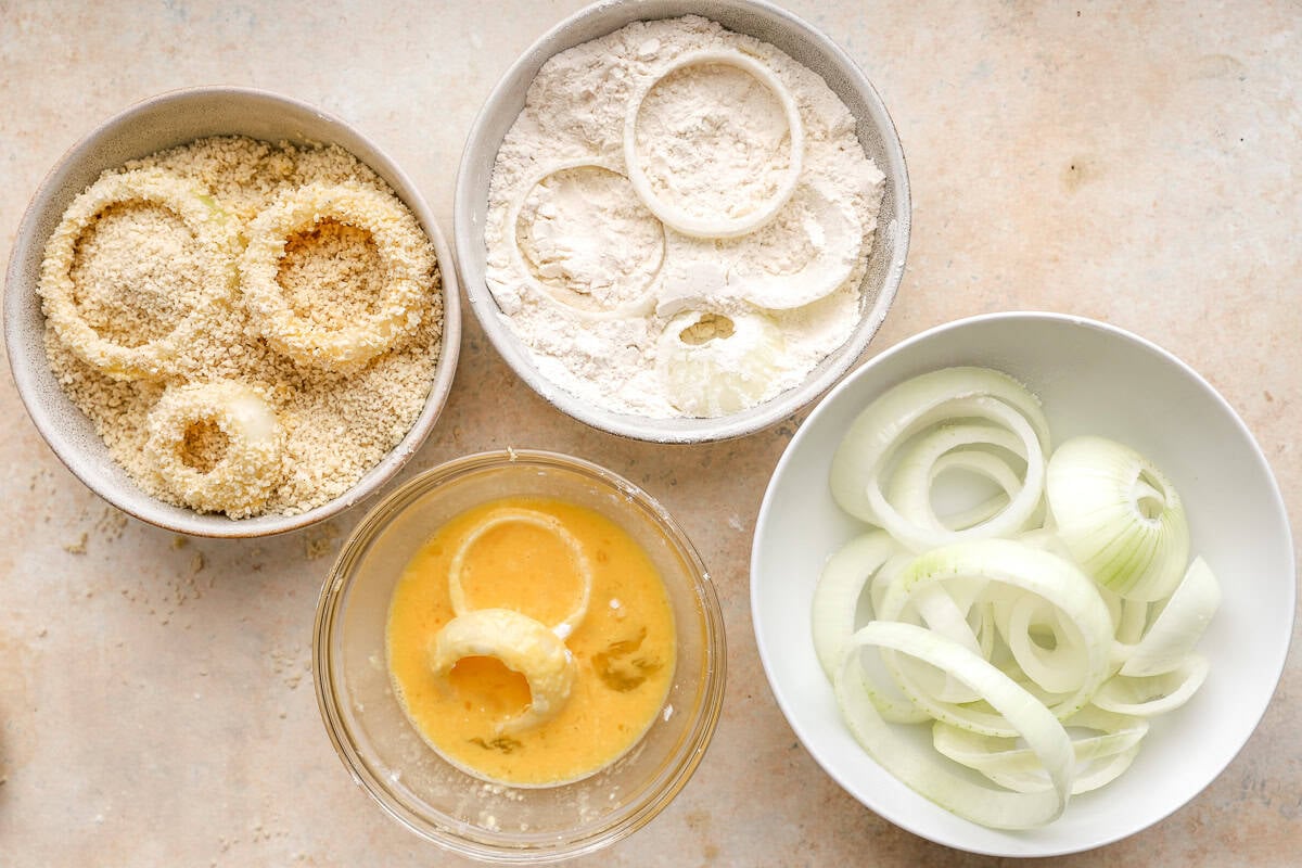 Step-by-step dredging station showing onion rings coated in flour, dipped in egg, and covered in panko breadcrumbs.