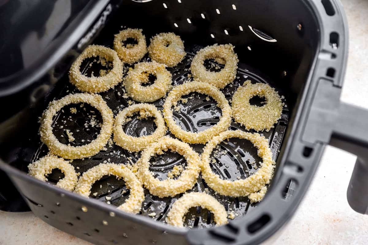 Uncooked panko-coated onion rings arranged in a single layer in the air fryer basket before cooking.