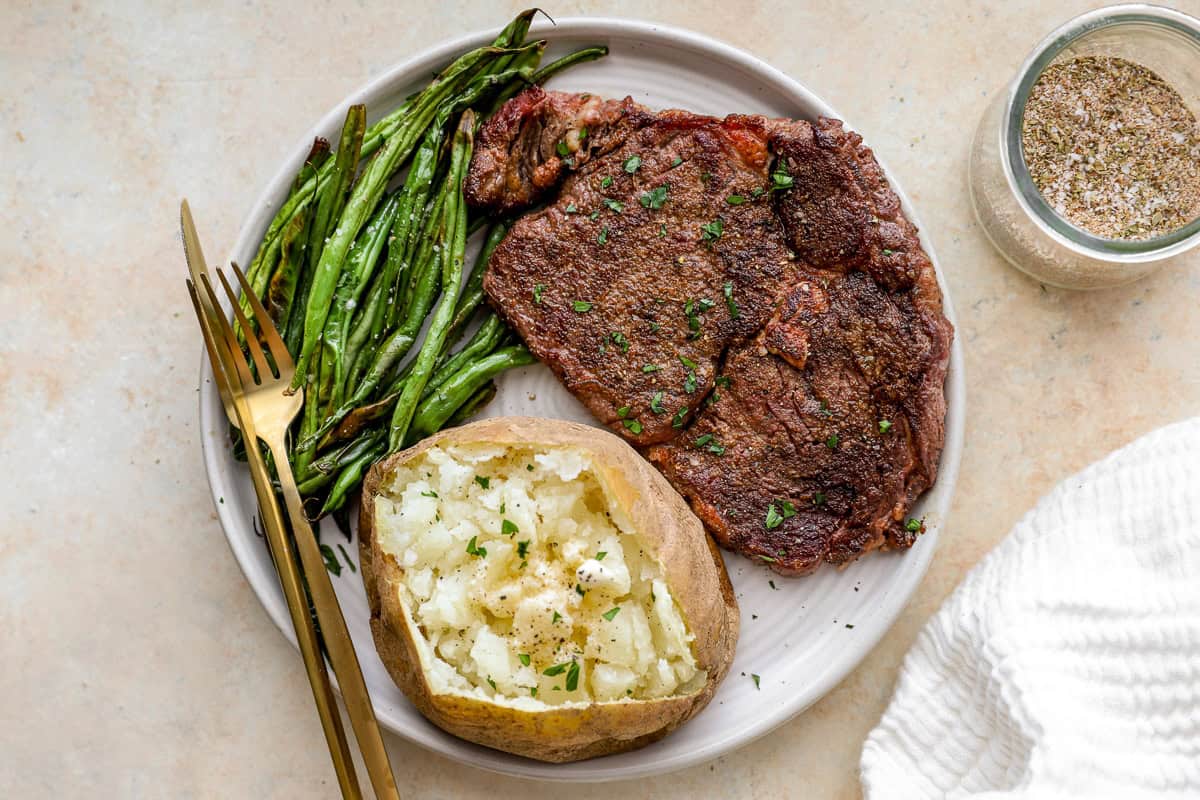 steak, baked potato and green beans cooked up on a plate