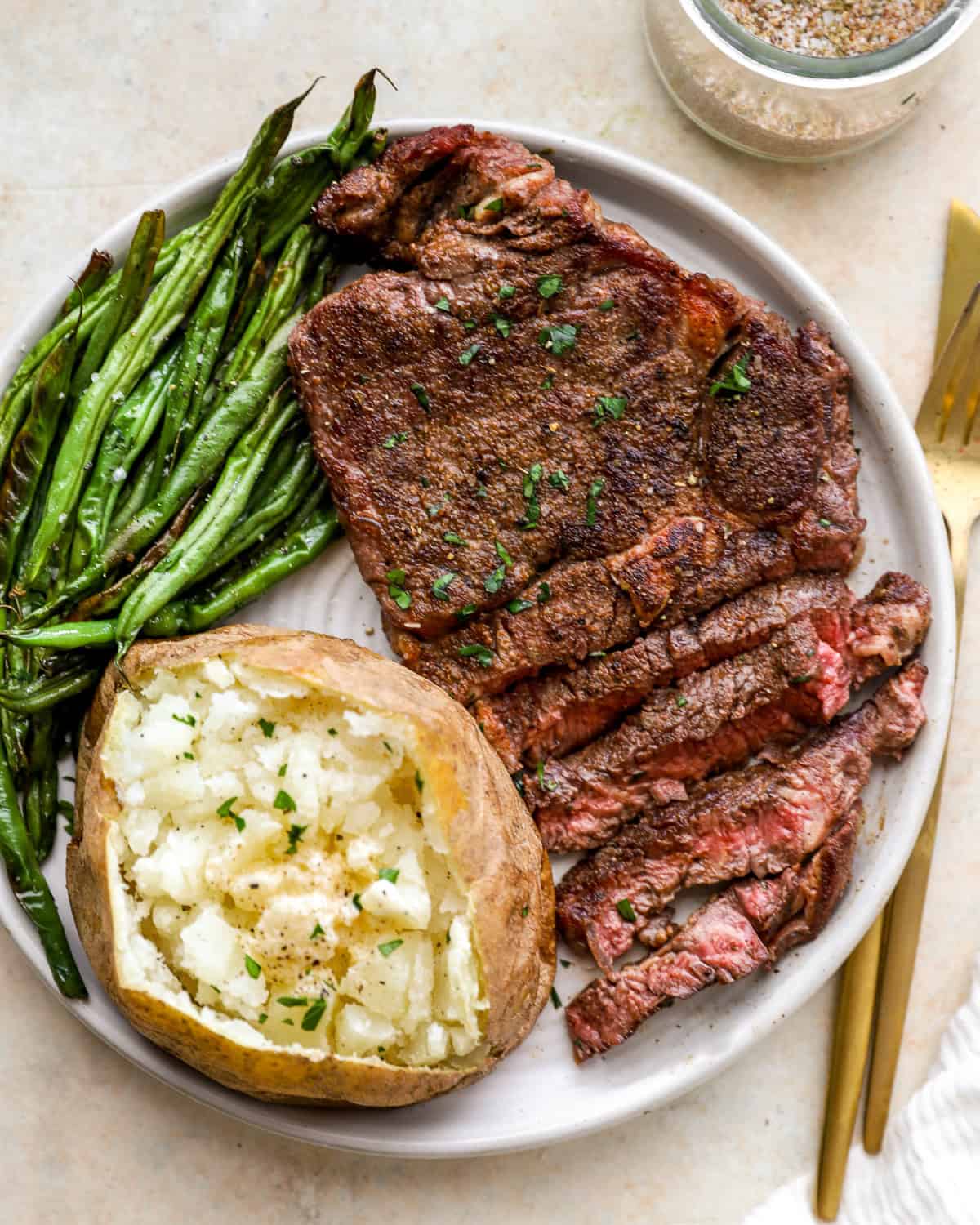 steak, baked potato and green beans cooked up on a plate