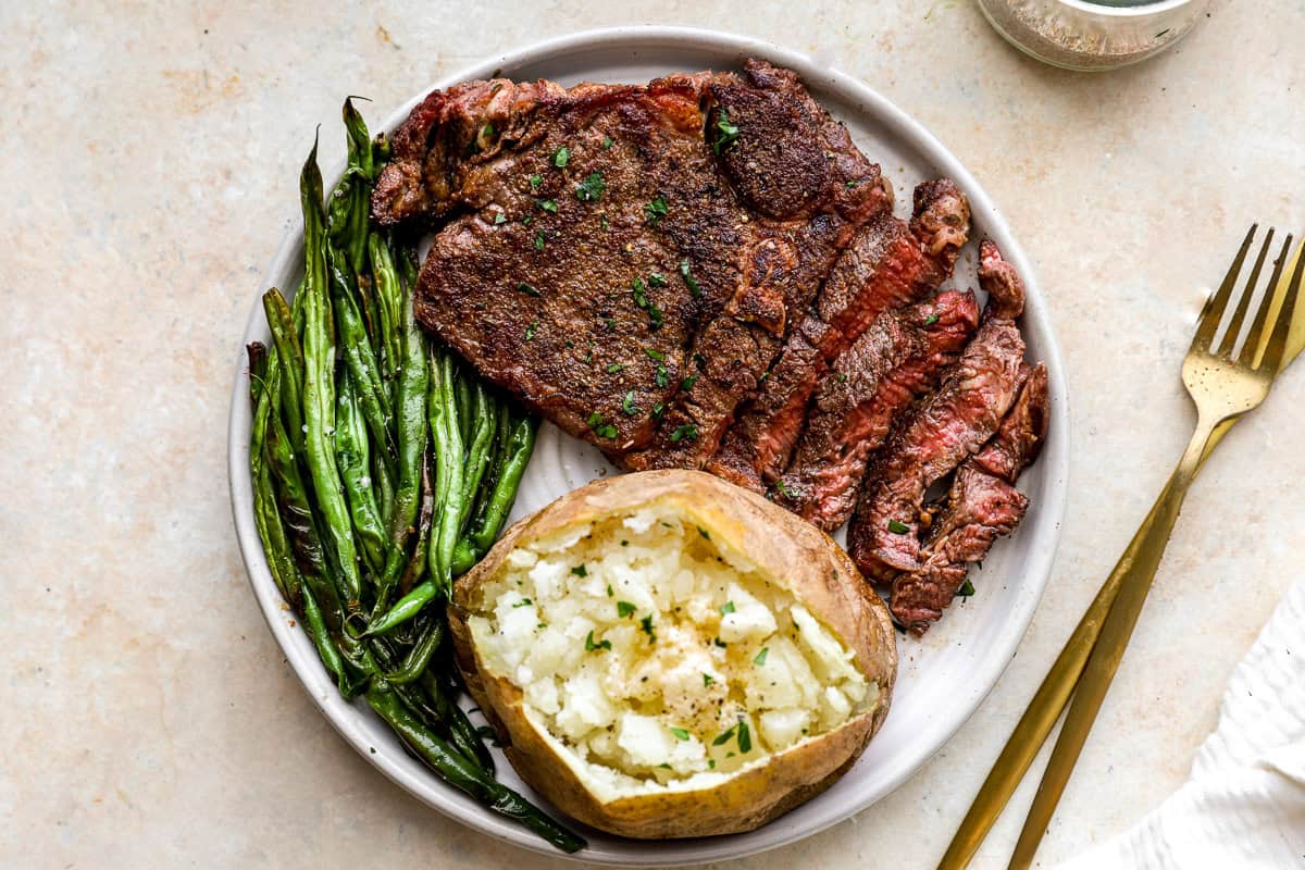 steak, baked potato and green beans cooked up on a plate