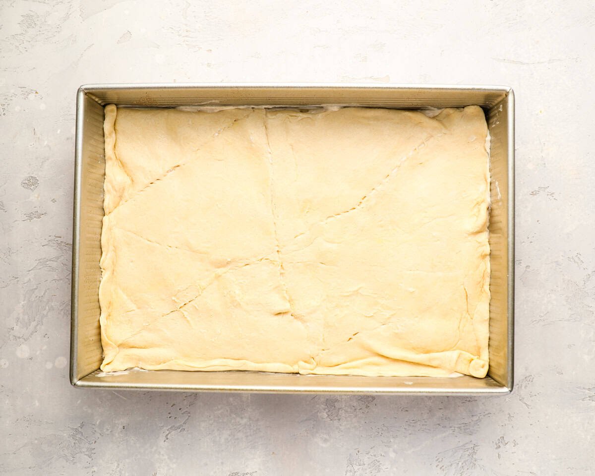 The top crescent dough sheet placed over the cheesecake filling in a 9x13 pan, edges pressed in.