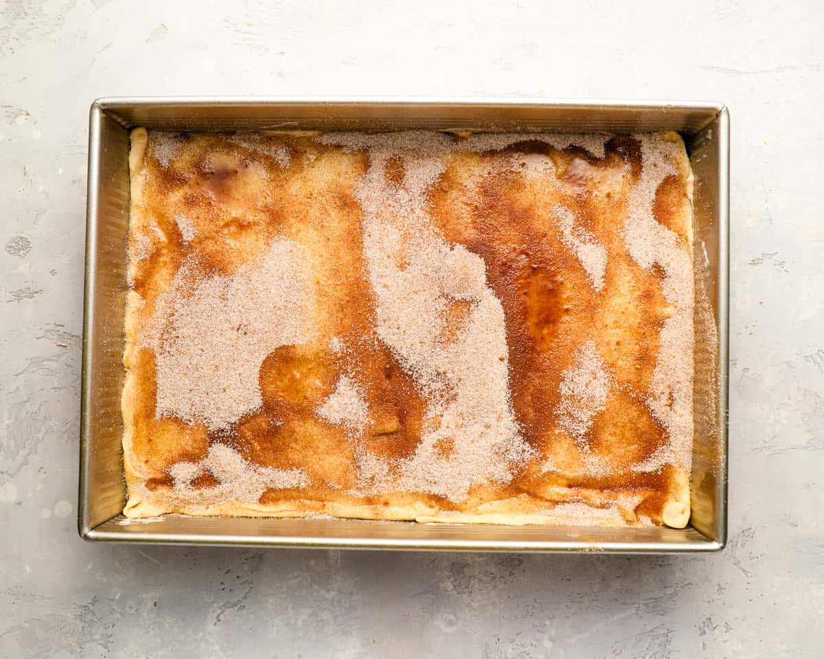 The top crescent dough brushed with melted butter and sprinkled with cinnamon sugar before baking.