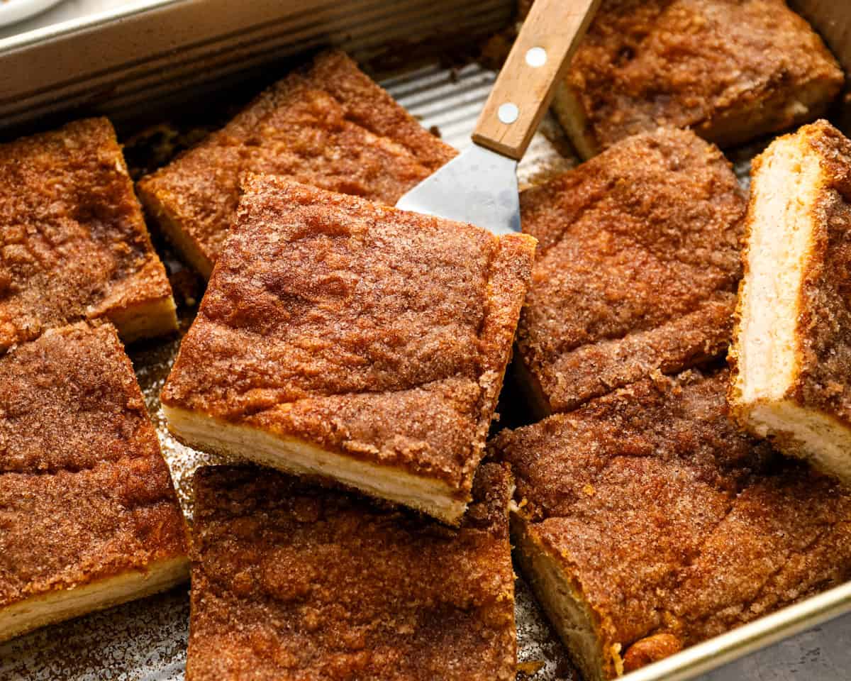 liced churro cheesecake bars in the pan with a spatula lifting one piece.