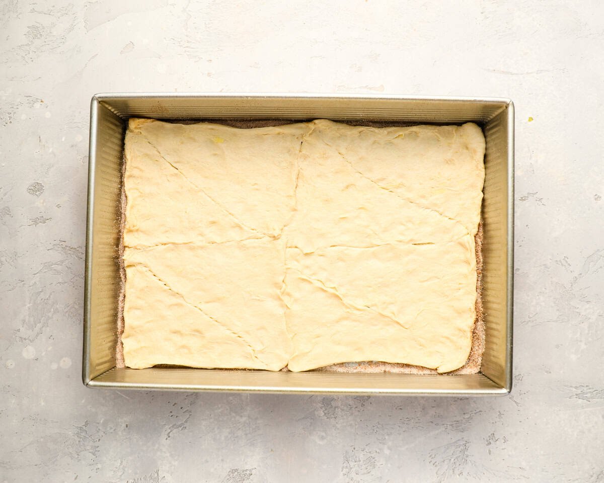 The bottom crescent dough sheet pressed into a 9x13 baking pan over the cinnamon sugar layer.