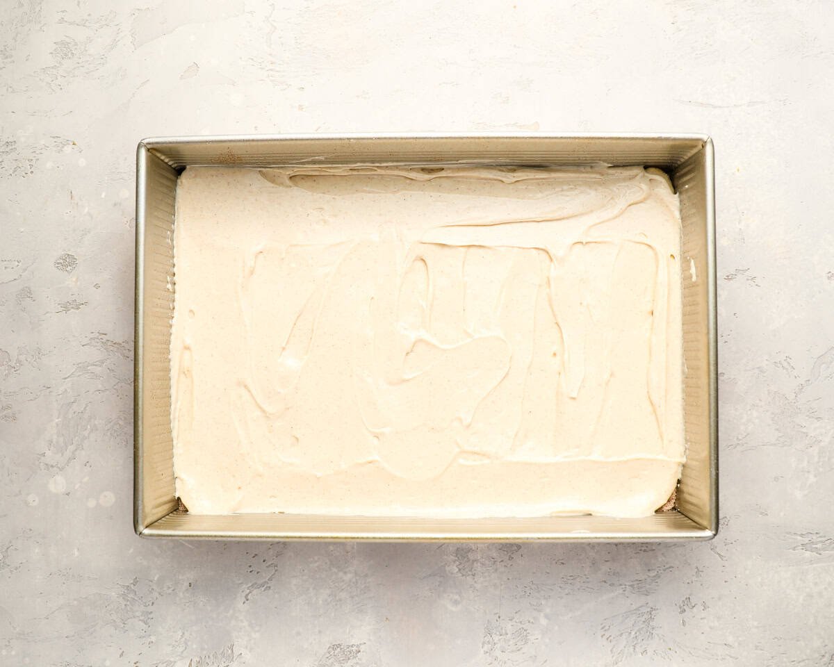 Cream cheese filling spread evenly over the bottom crescent dough layer in a baking pan.