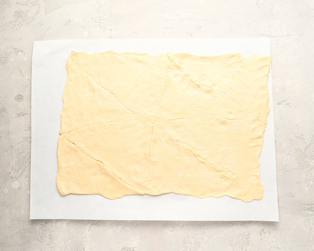 A full sheet of crescent dough stretched out on parchment paper, seams pinched together.