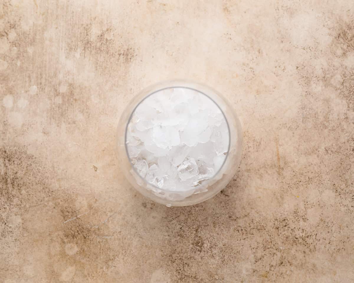 A top view of a stemless glass filled halfway with crushed ice on a neutral stone surface.