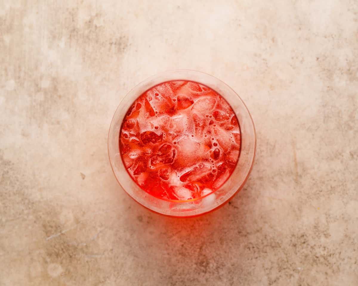 A top view of the cranberry Aperol spritz mixture poured over crushed ice, showing the bright red color.
