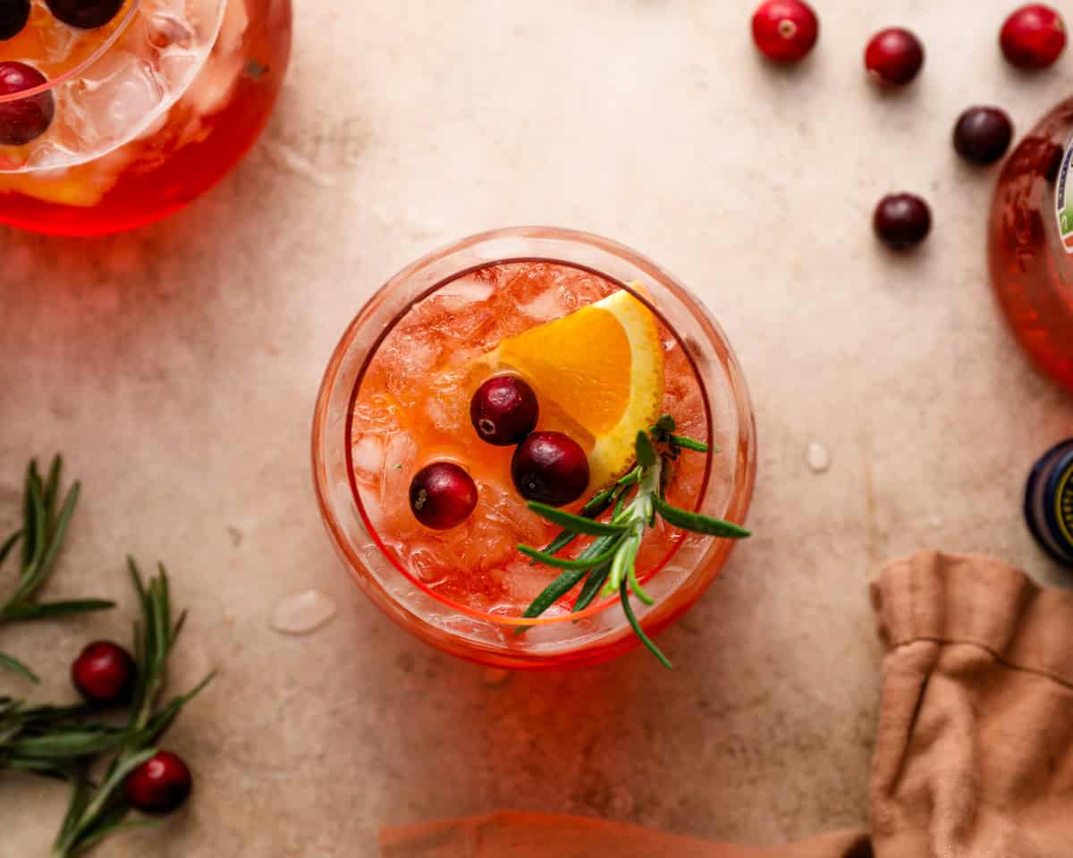 A top view of a finished cranberry Aperol spritz garnished with an orange wedge, cranberries, and fresh rosemary.