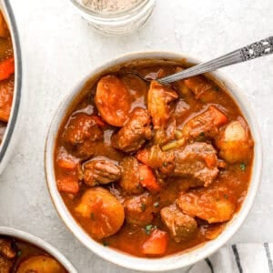 A bowl of hearty beef stew filled with tender beef chunks, carrots, potatoes, and celery in a rich broth, with a jar of homemade beef stew seasoning beside it.
