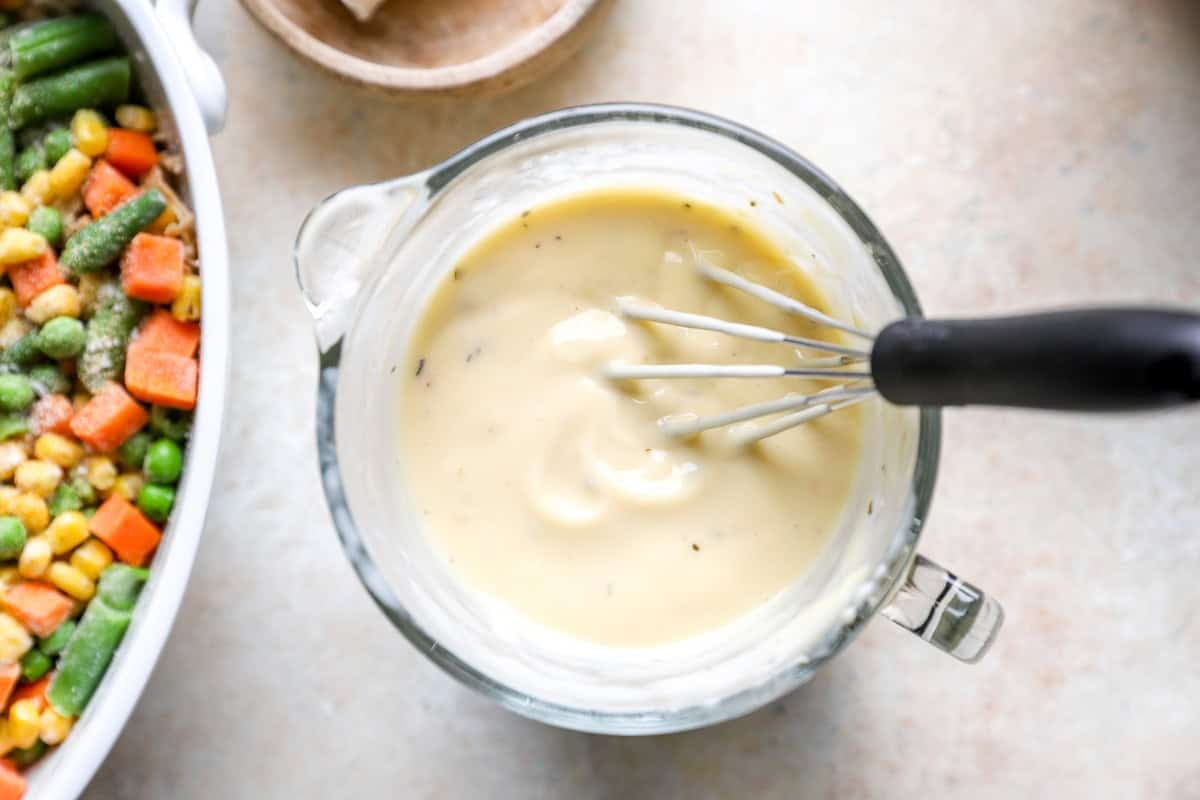 Creamy mixture of cream of chicken soup and milk being whisked together in a glass measuring cup.