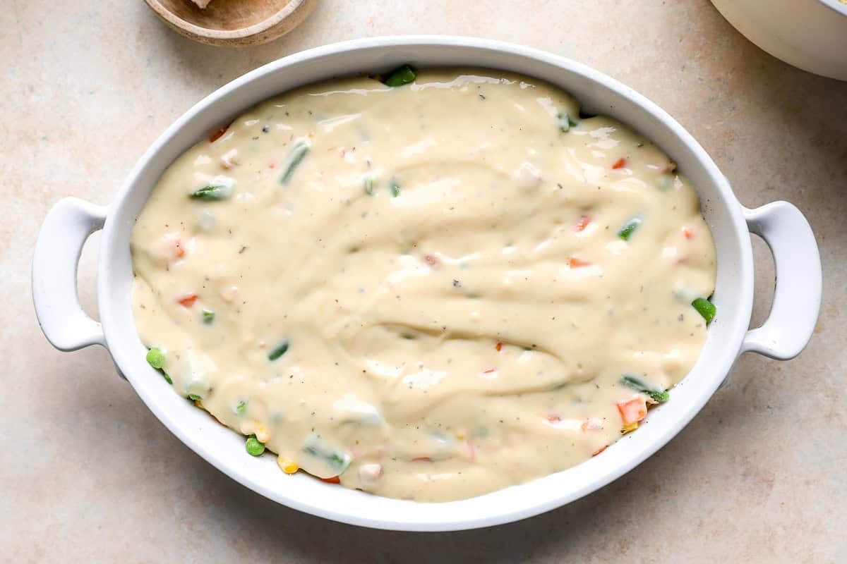 Casserole dish filled with chicken, vegetables, and a smooth layer of cream of chicken sauce spread evenly on top.