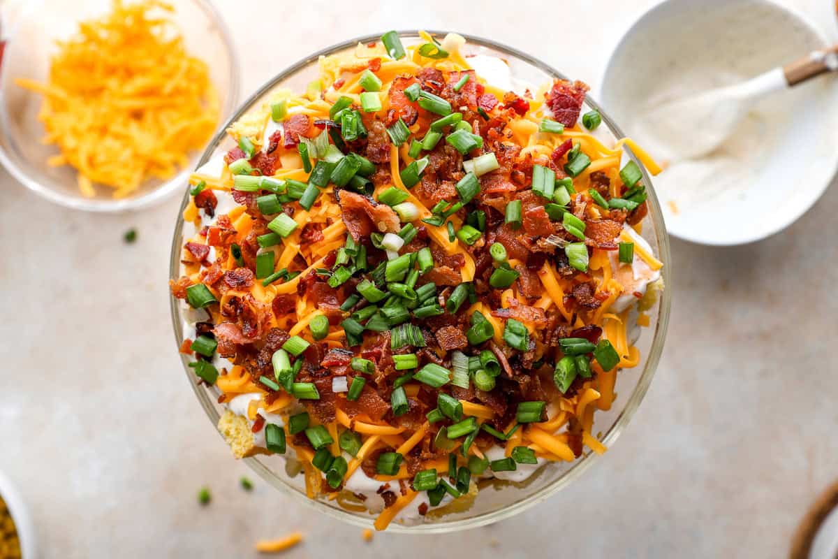 Overhead view of cornbread salad topped with shredded cheddar, crispy bacon crumbles, and chopped green onions.