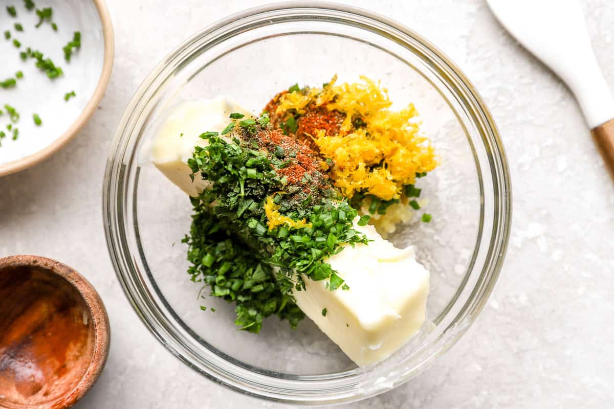 Softened butter, fresh herbs, lemon zest, garlic, and spices in a glass mixing bowl before combining.