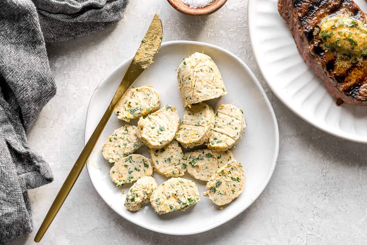 Sliced coins of cowboy compound butter on a plate next to grilled steak.
