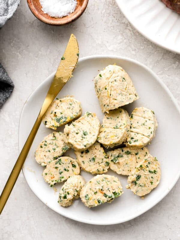 Slices of chilled cowboy compound butter on a white plate with a gold butter knife.