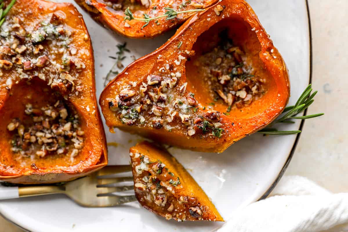 Roasted honeynut squash served on a plate with herbs and pecans, with a bite cut and resting on a fork.