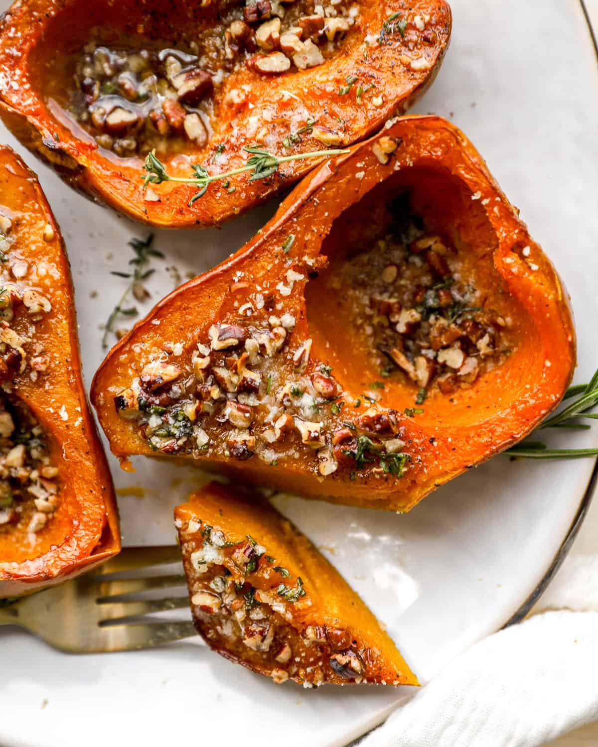 Roasted honeynut squash halves topped with toasted pecans, herb butter, and Parmesan on a white plate.