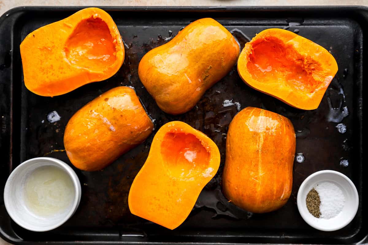 Halved honeynut squash brushed with butter and seasoned with salt and pepper on a baking sheet.