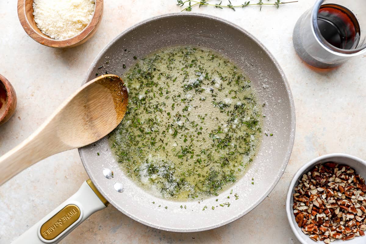 Skillet with melted butter mixed with chopped rosemary, thyme, and garlic, wooden spoon resting in the pan.