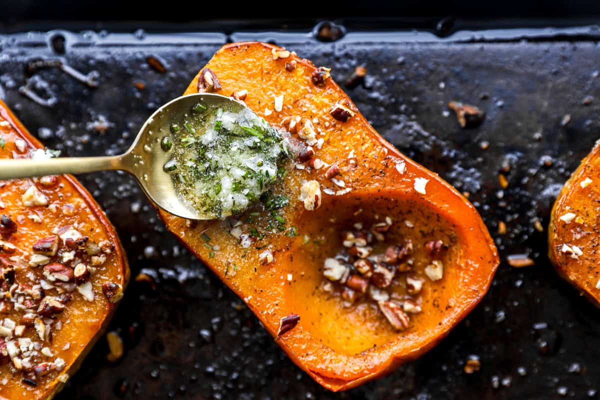 A spoon drizzling warm herb and garlic butter over roasted honeynut squash topped with pecans.