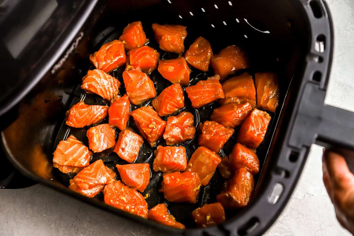 Marinated salmon pieces arranged in a single layer inside an air fryer basket before cooking.