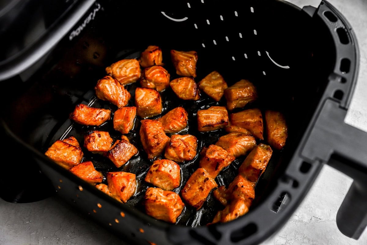 Air fryer basket filled with cooked salmon bites that are golden brown with caramelized edges.