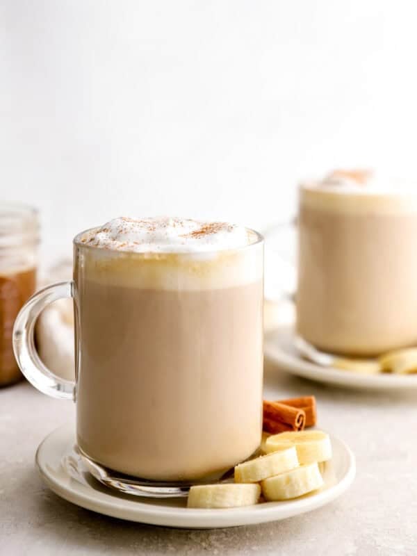 Banana bread latte topped with frothy milk and cinnamon, served in a glass mug with sliced banana and cinnamon sticks