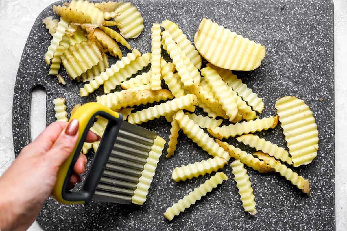 Hand slicing gold potatoes into crinkle cut fries using a crinkle cutter on a cutting board
