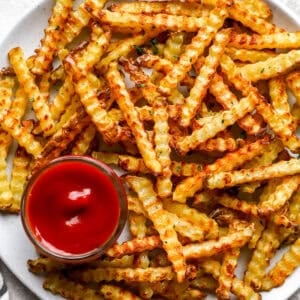 Golden oven baked crinkle cut fries served on a white plate with a small bowl of ketchup