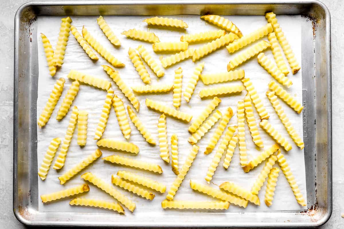 Crinkle cut fries arranged in a single layer on a parchment lined baking sheet before baking