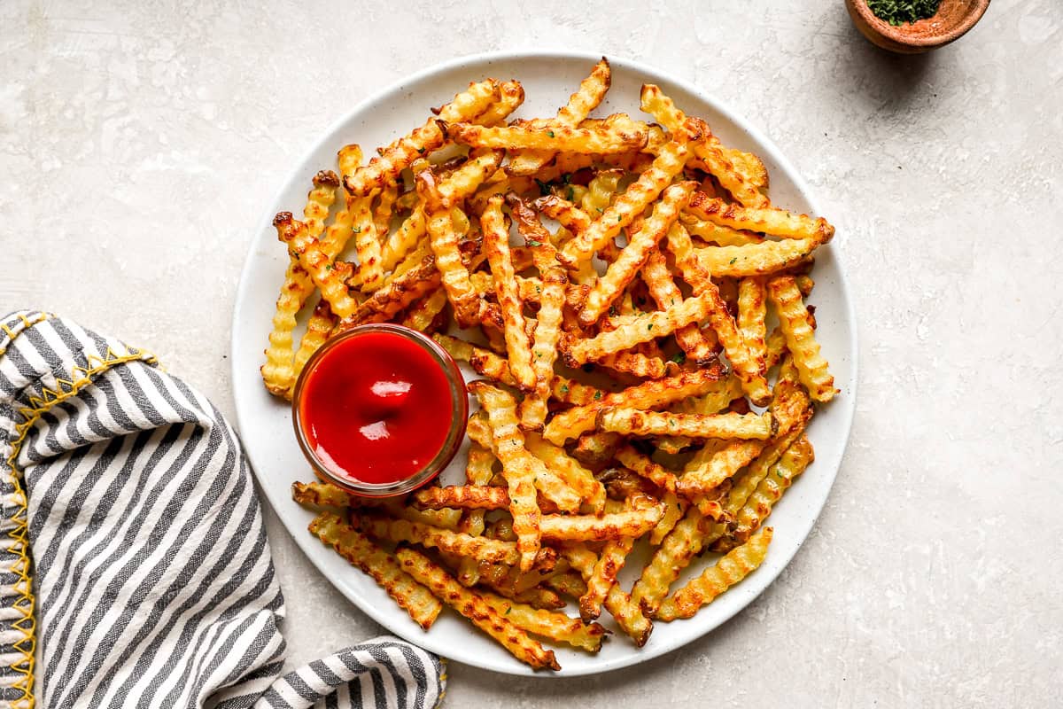 Plate of crispy crinkle cut fries served with ketchup and a kitchen towel on the side