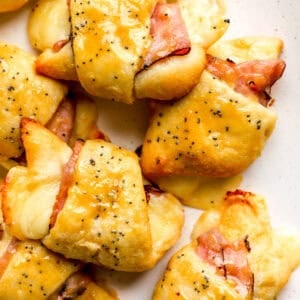 Finished ham and cheese croissants on a plate, golden brown with melted Swiss cheese and poppy seed topping