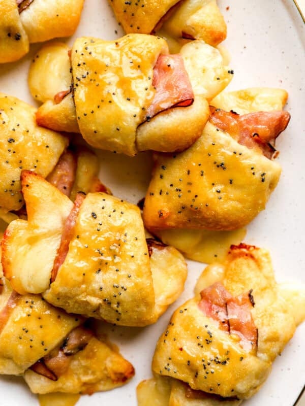 Finished ham and cheese croissants on a plate, golden brown with melted Swiss cheese and poppy seed topping